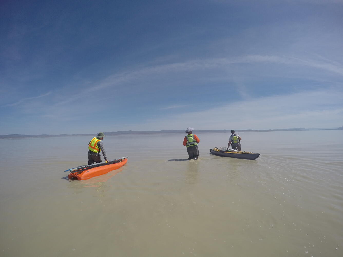 researchers wading in the lake with boats full of gear in tow behind them