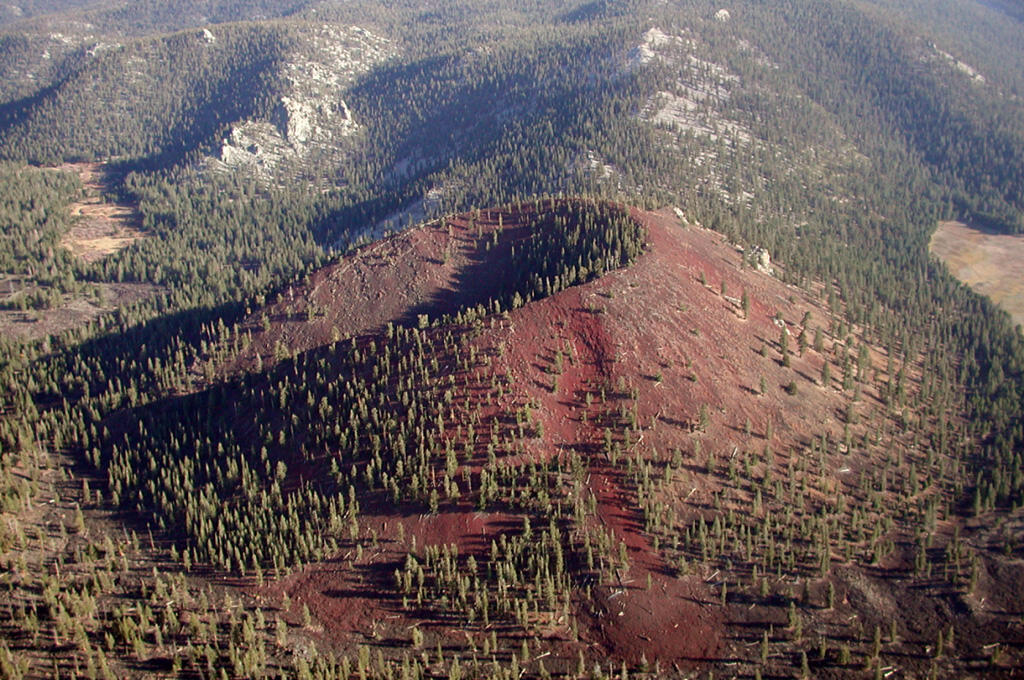 A red scoria cone is dotted with pine forest and sits on the valley floor near low hills of bright white Sierra Nevada granite. 
