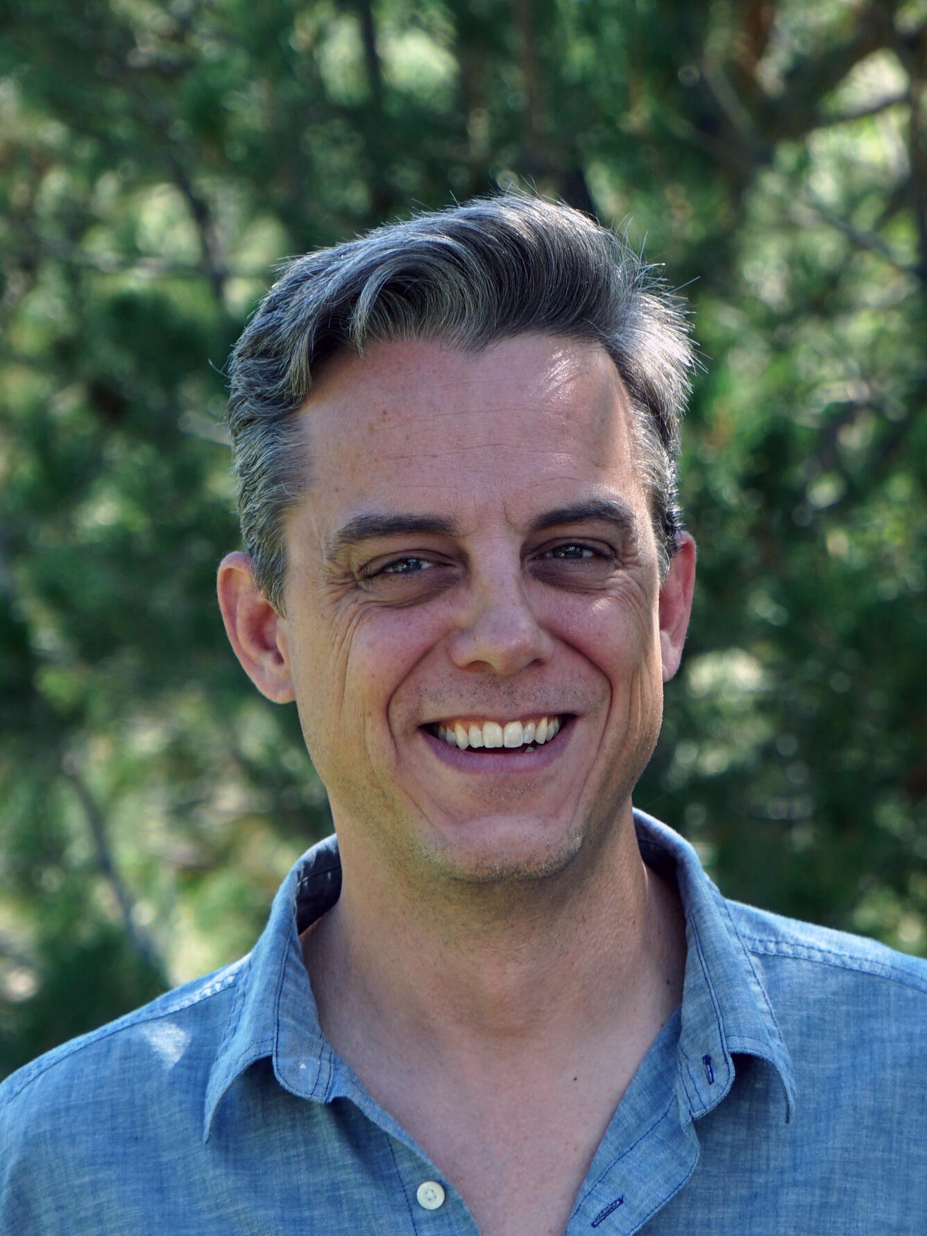 man wearing a gray shirt standing near trees