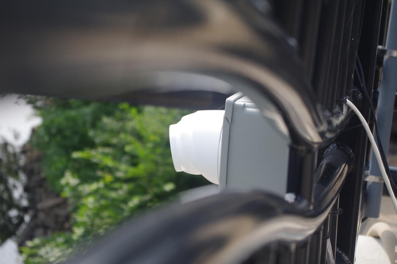 White web camera housing viewed through black fencing