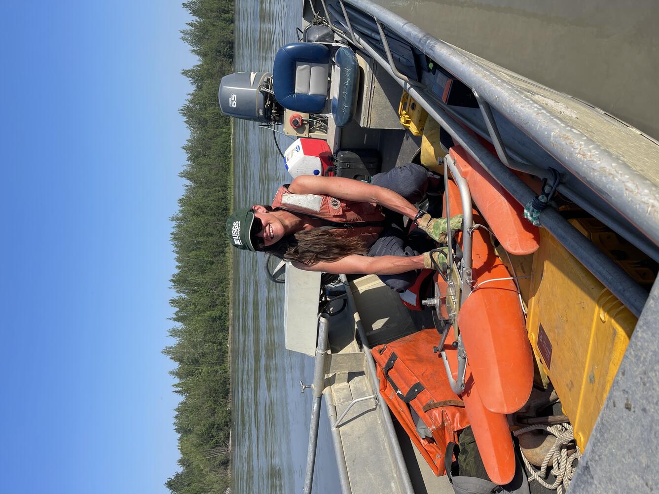 Hydrologist in small aluminum boat on Nenana River. Has USGS hat and float vest on. Launching field equipment on the river. 