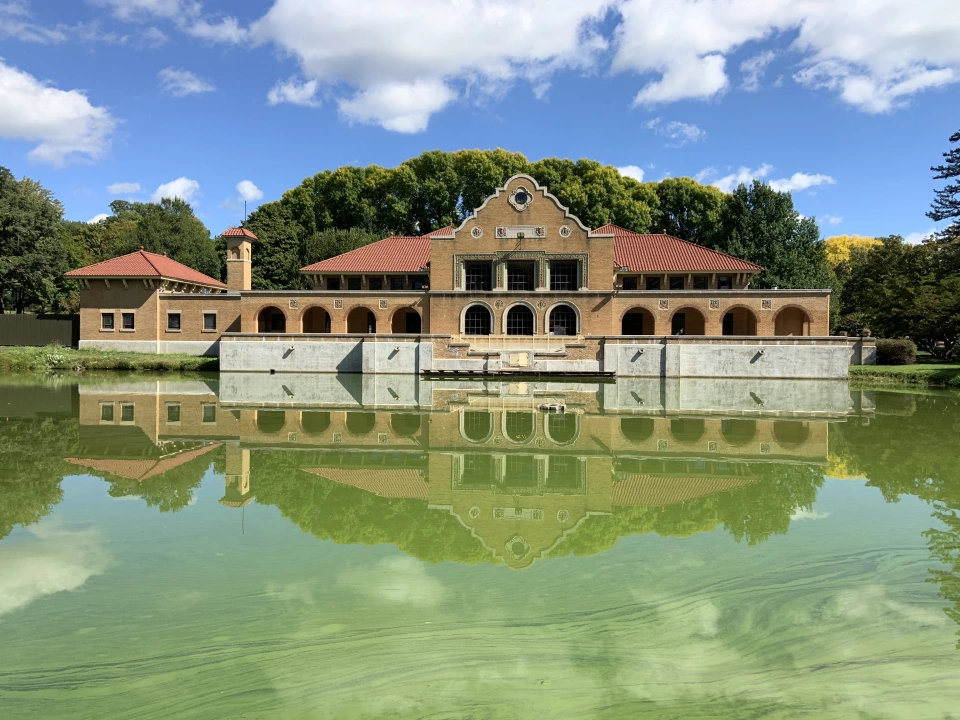 The Spanish Revival style Washington Park Lakehouse is reflected in murky green lake waters on a mostly sunny day