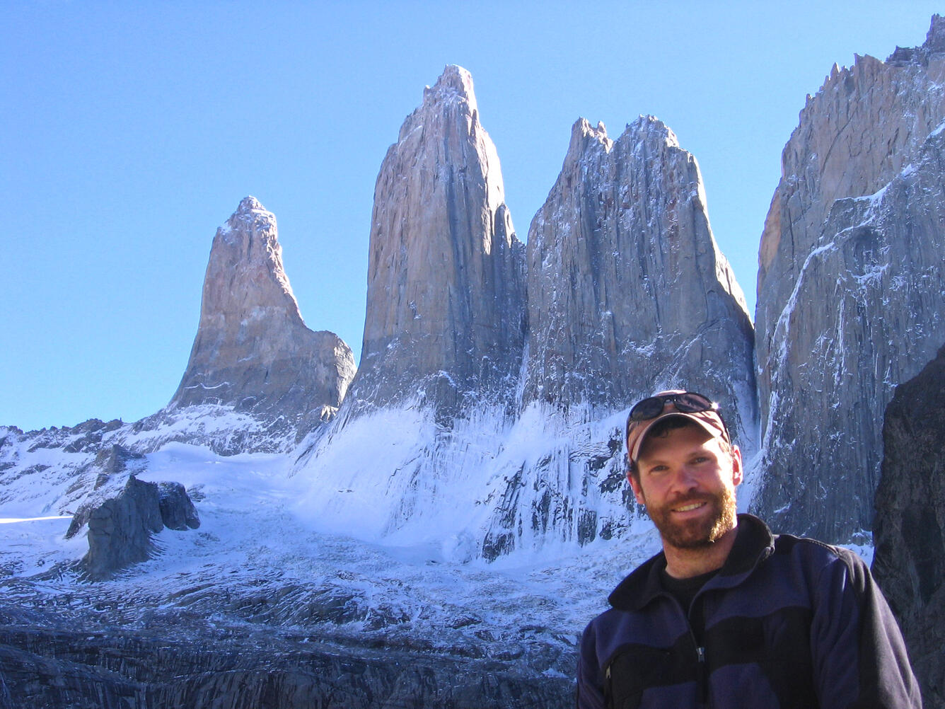 male scientist, wearing a black sweatshirt, red hat, standing near mountains
