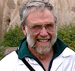 Headshot of a white-haired man wearing glasses, smiling broadly