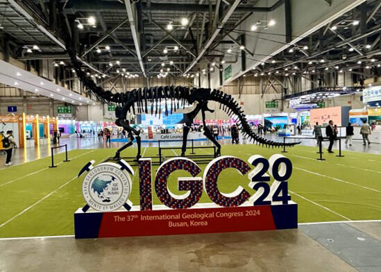Sign for the 2024 International Geologic Congress, in front of a display skeleton of a long-necked dinosaur.