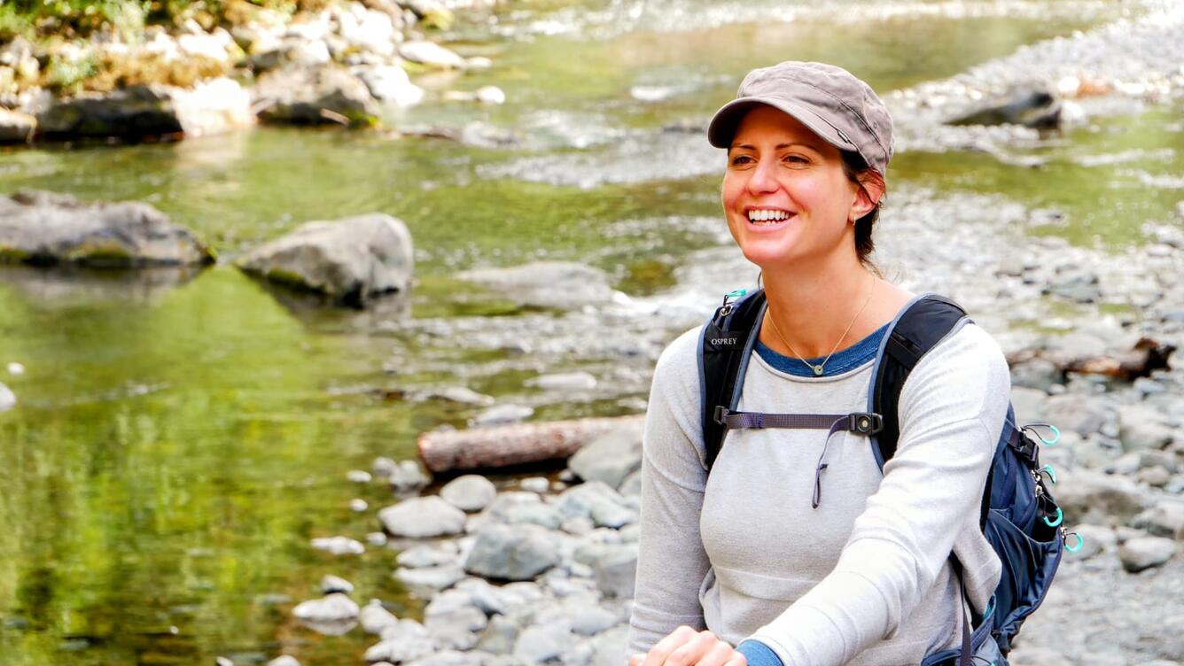 photo of woman smiling and standing near a creek