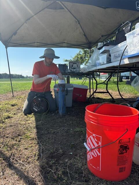Scientist lowers a tape into a well with buckets and equipment waiting in the foreground