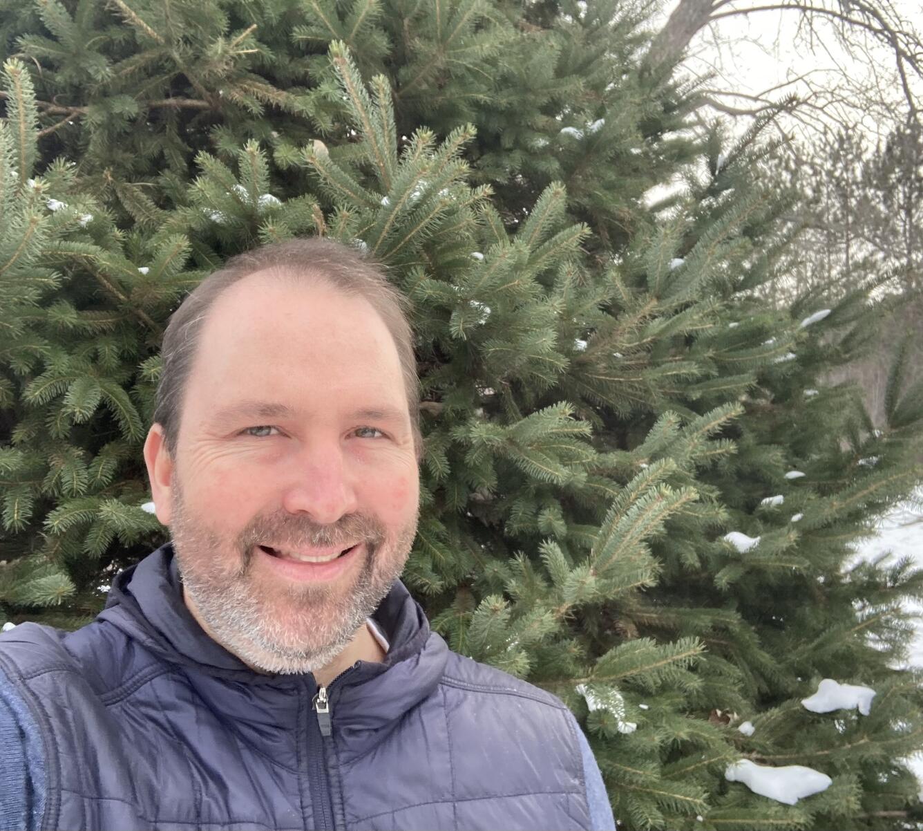 man standing near an evergreen tree wearing a blue jacket