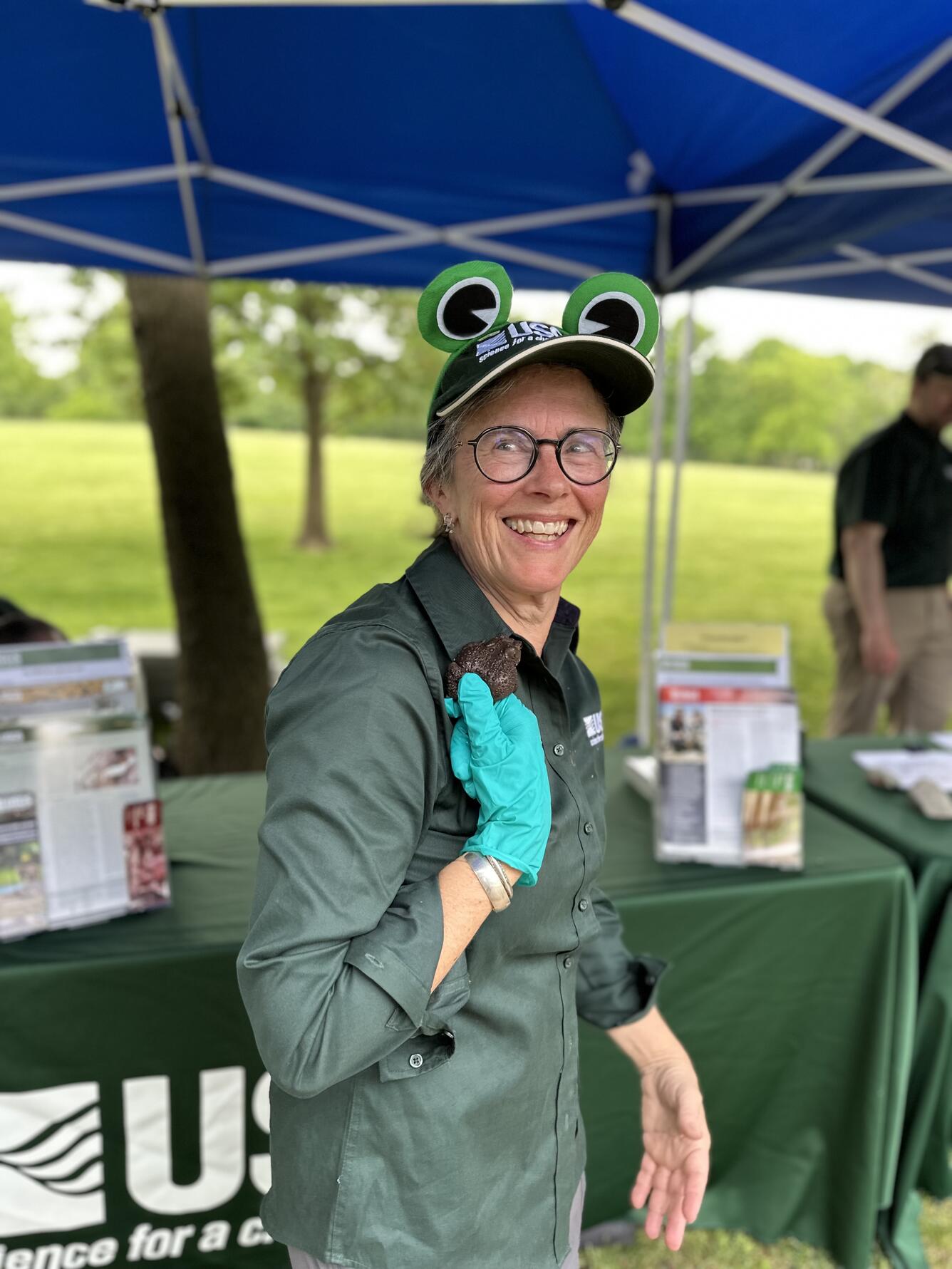 A woman wearing clothing labeled with USGS holds a toad and smiles giddily