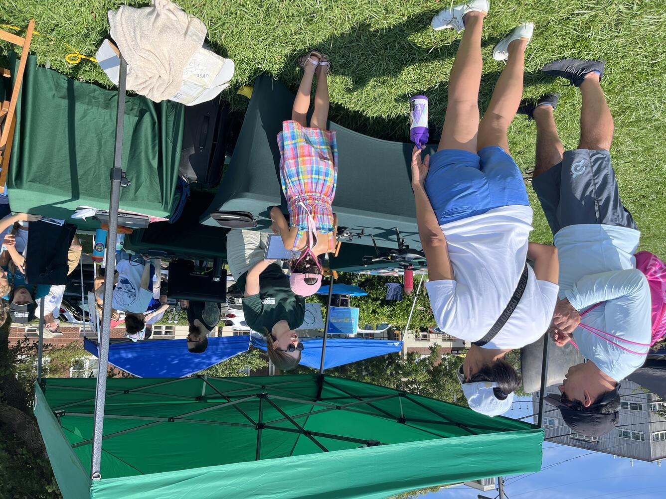 USGS scientist standing behind table, under tent, outside, showing drones and talking to a child and two adults.