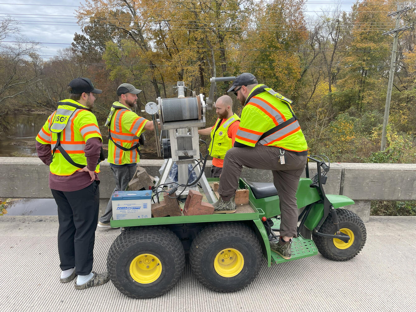 USGS scientists lowering a bedload sampler over the edge of a bridge.