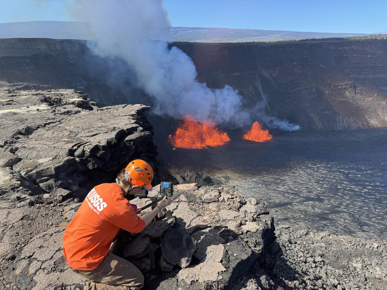 Color photograph of scientist checking monitoring equipment on volcano