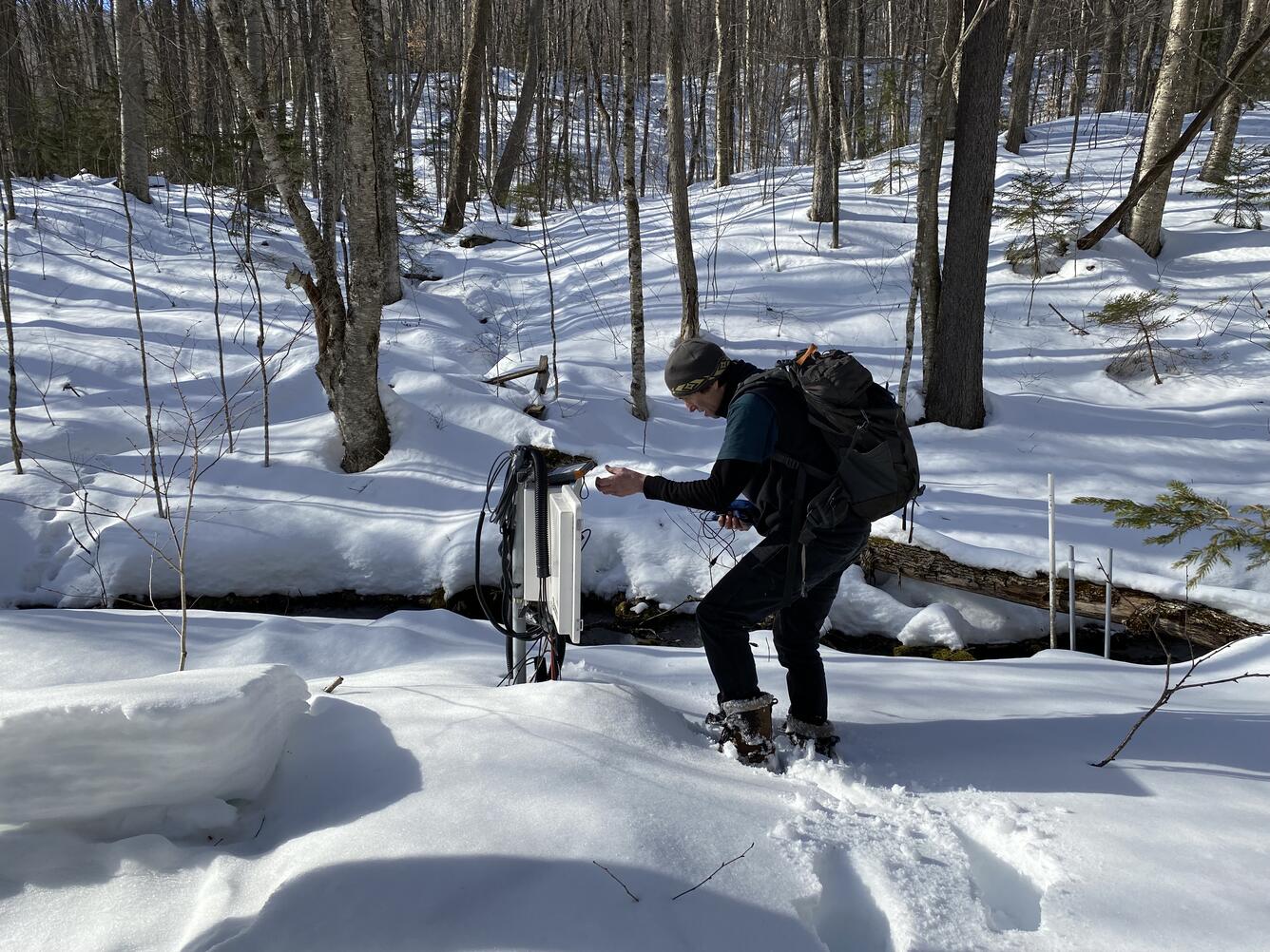 A man in the snowy woods looks at a data logger.