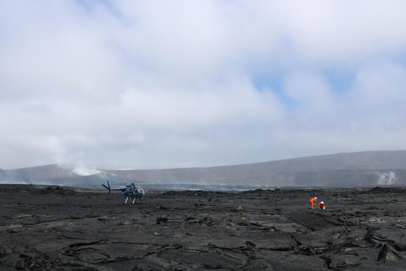 Color photograph of scientists working in volcanic crater with vent in background
