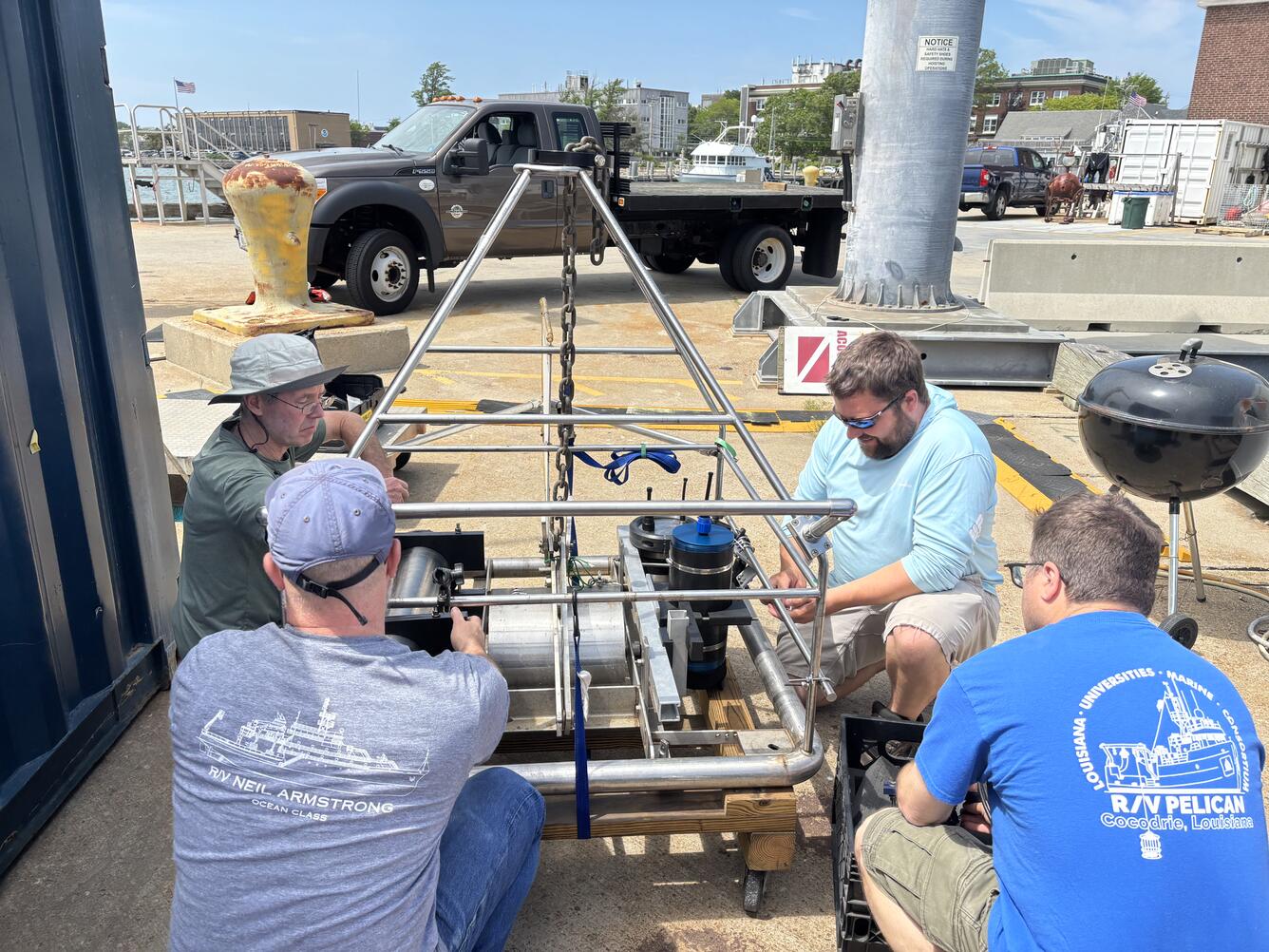 four people around a large piece of equipment outside by the water