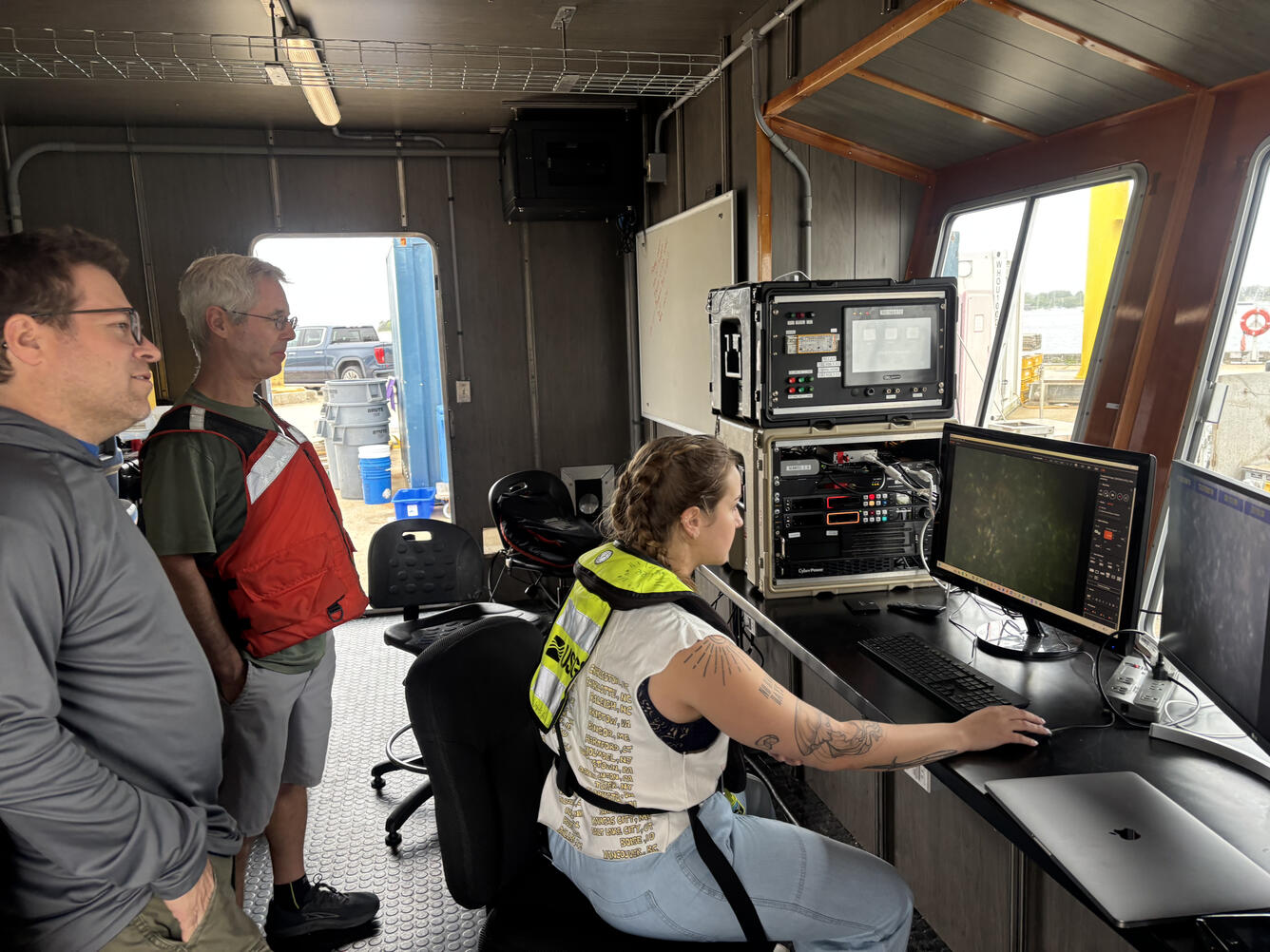 Three people staring at computer screens showing images of the seafloor