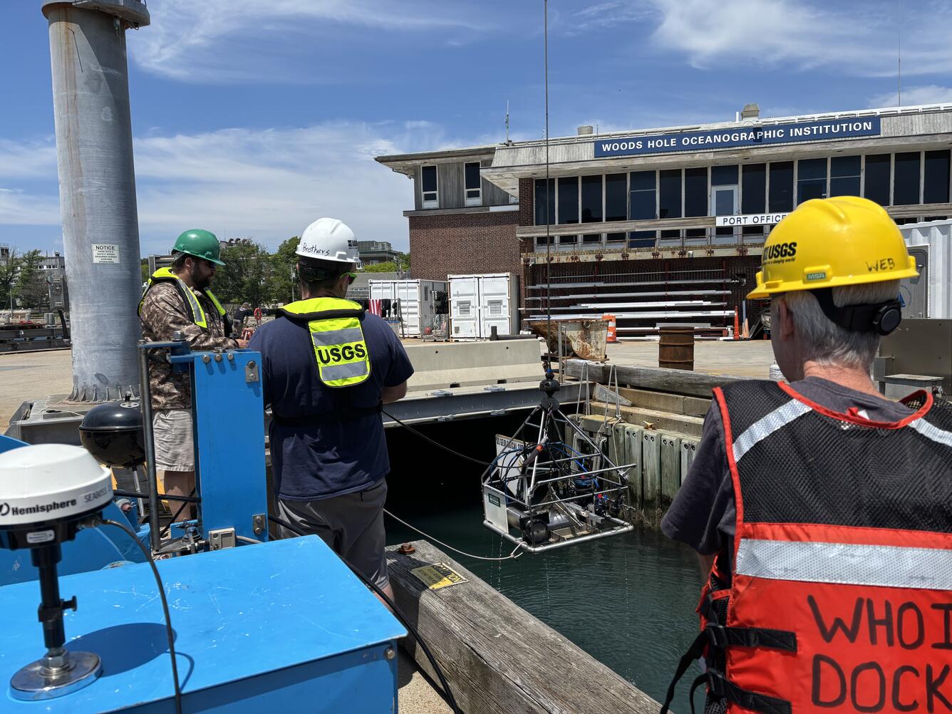 People on a dock lowering a big piece of equipment into the water