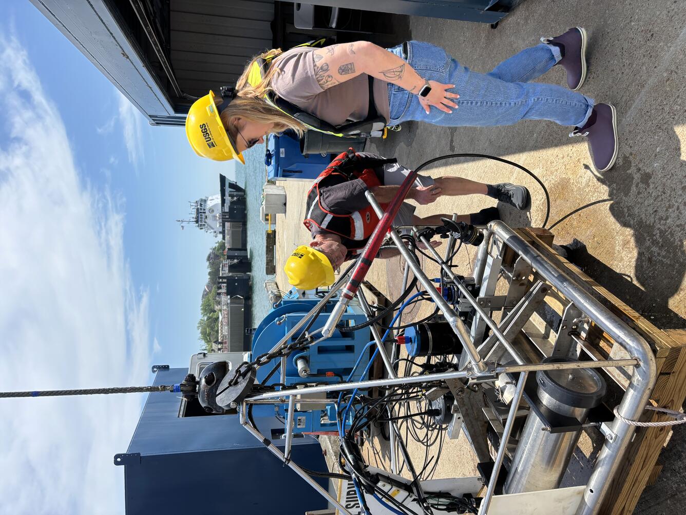 Two people inspecting a big piece of equipment on a dock outside