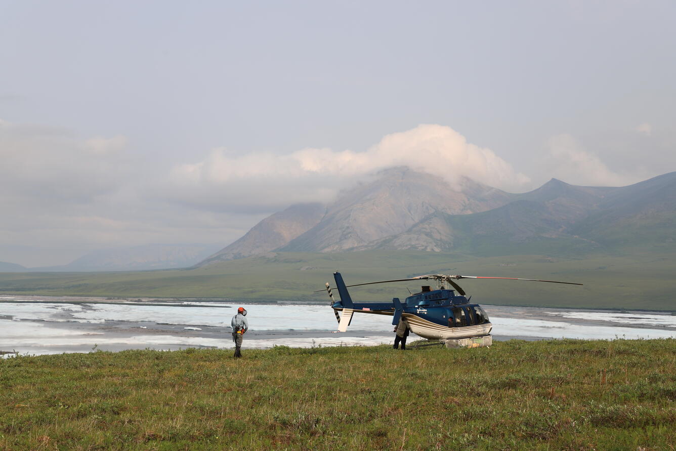two people near helicopter with mountains in the background
