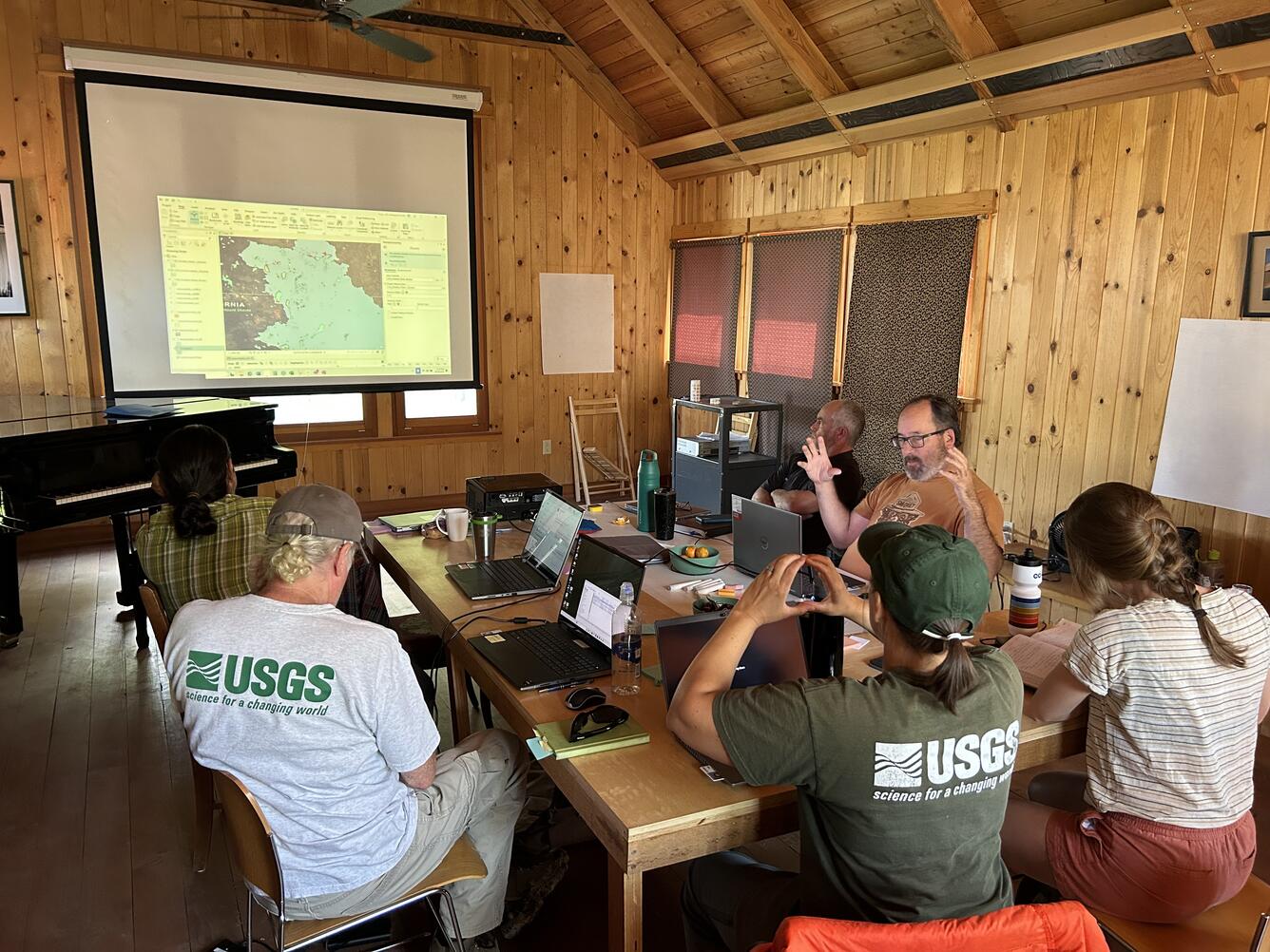 A group of seven researchers sits around a table in a wood-paneled room