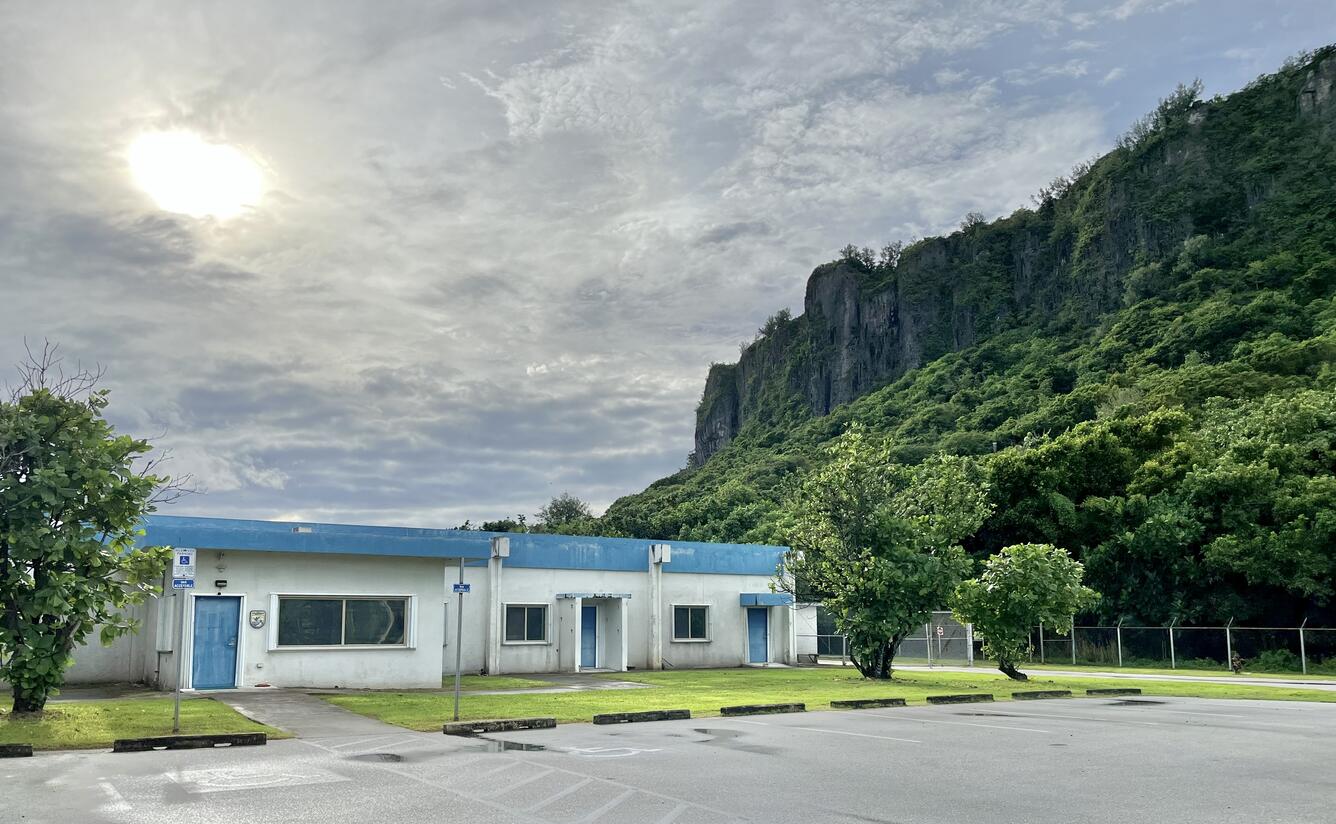 White and blue one-story building with tropical trees and cliffs