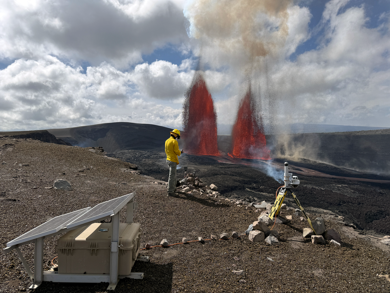 Two lava fountains erupt from vents on crater floor as scientist monitors in the foreground