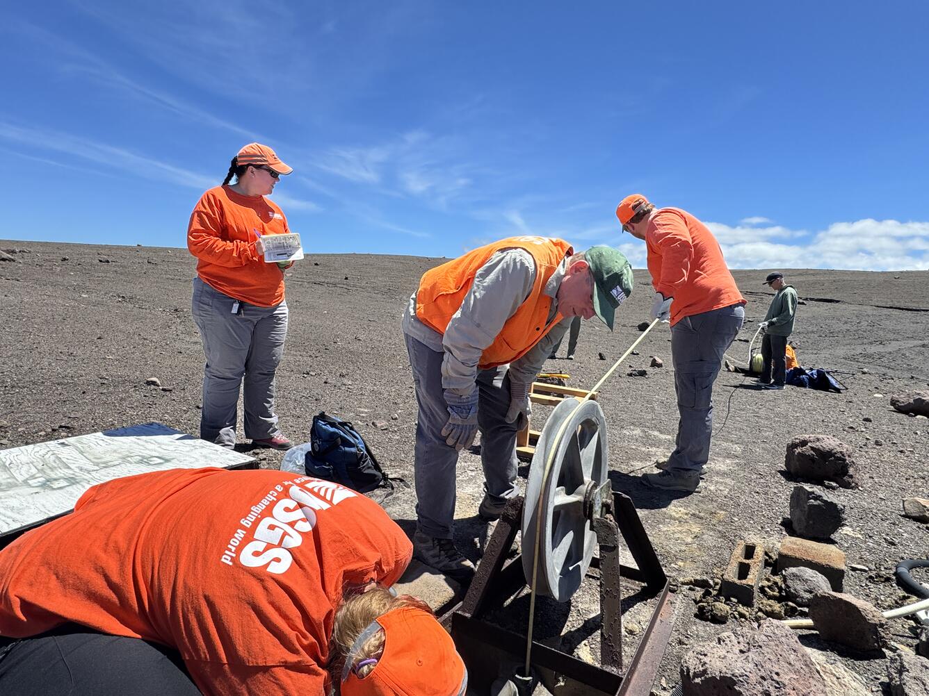 Several scientists working around a hole in the ground that is a well