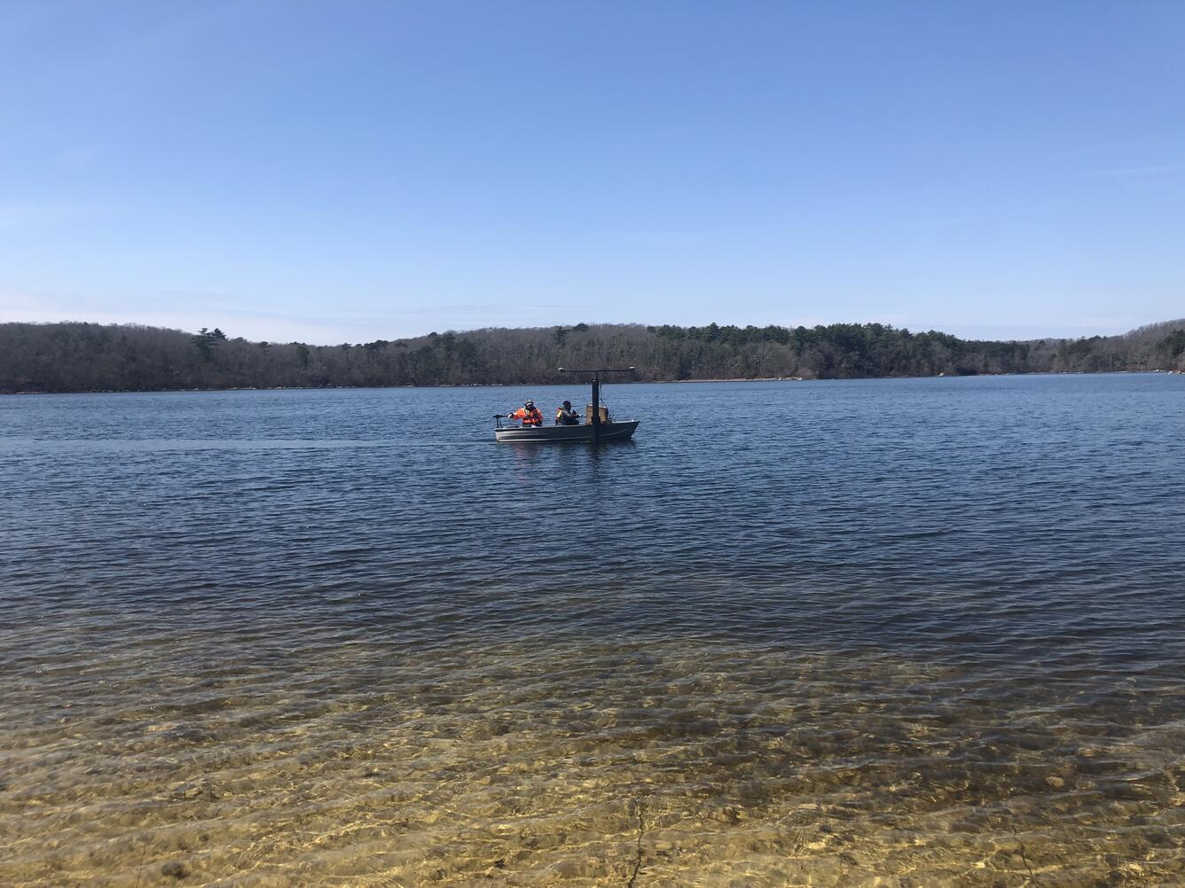 small boat on pond, trees lining the edge of the pond