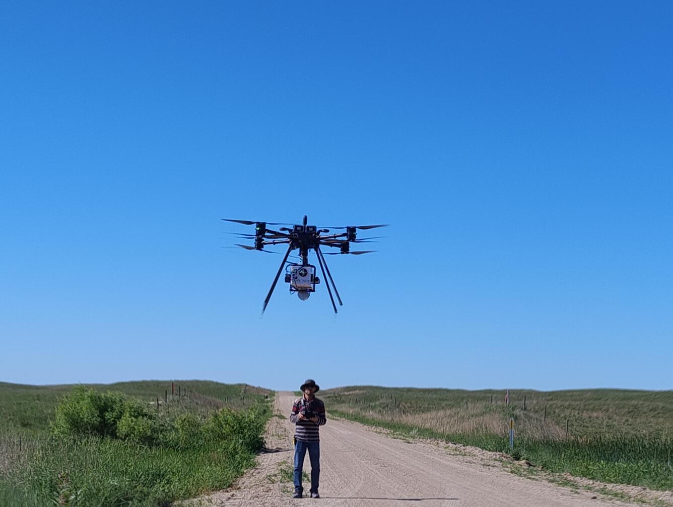 A person operates a drone in a grassland prairie
