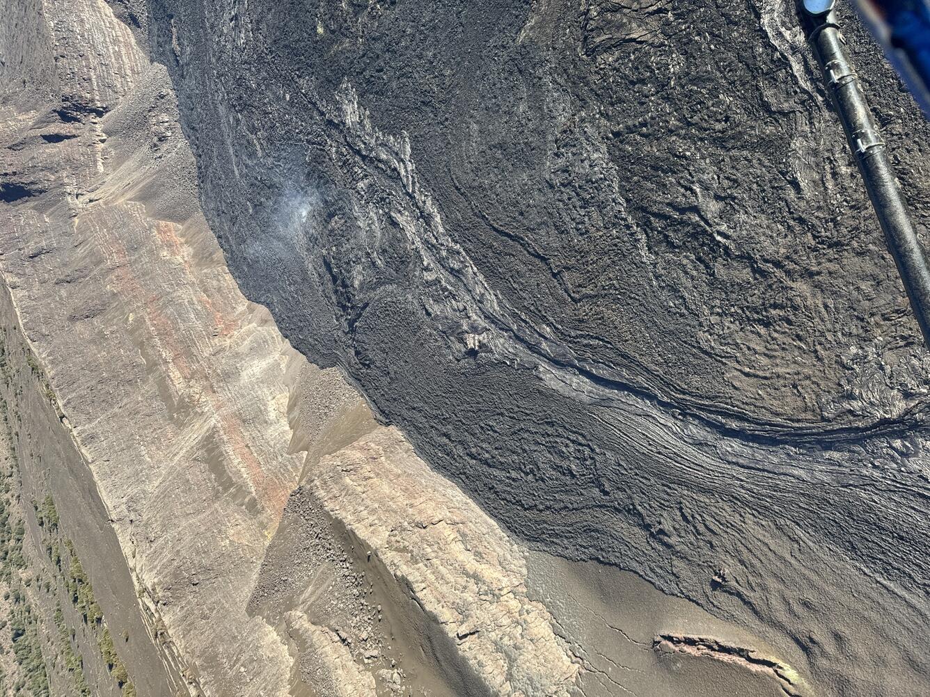 Color photograph of solidified lava channel next to crater wall