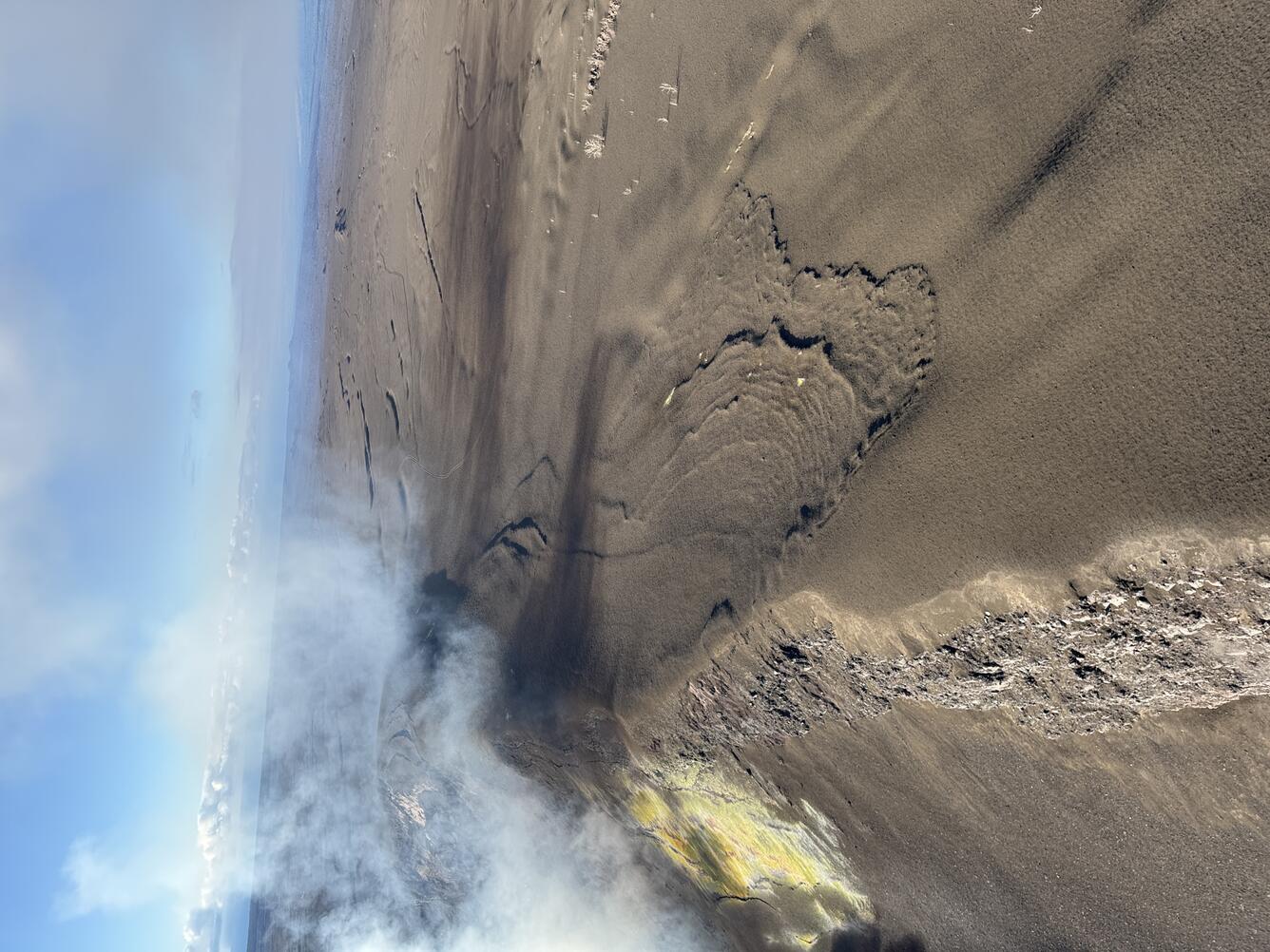 Color photograph showing volcanic gas wafting over a tephra-blanketed crater rim