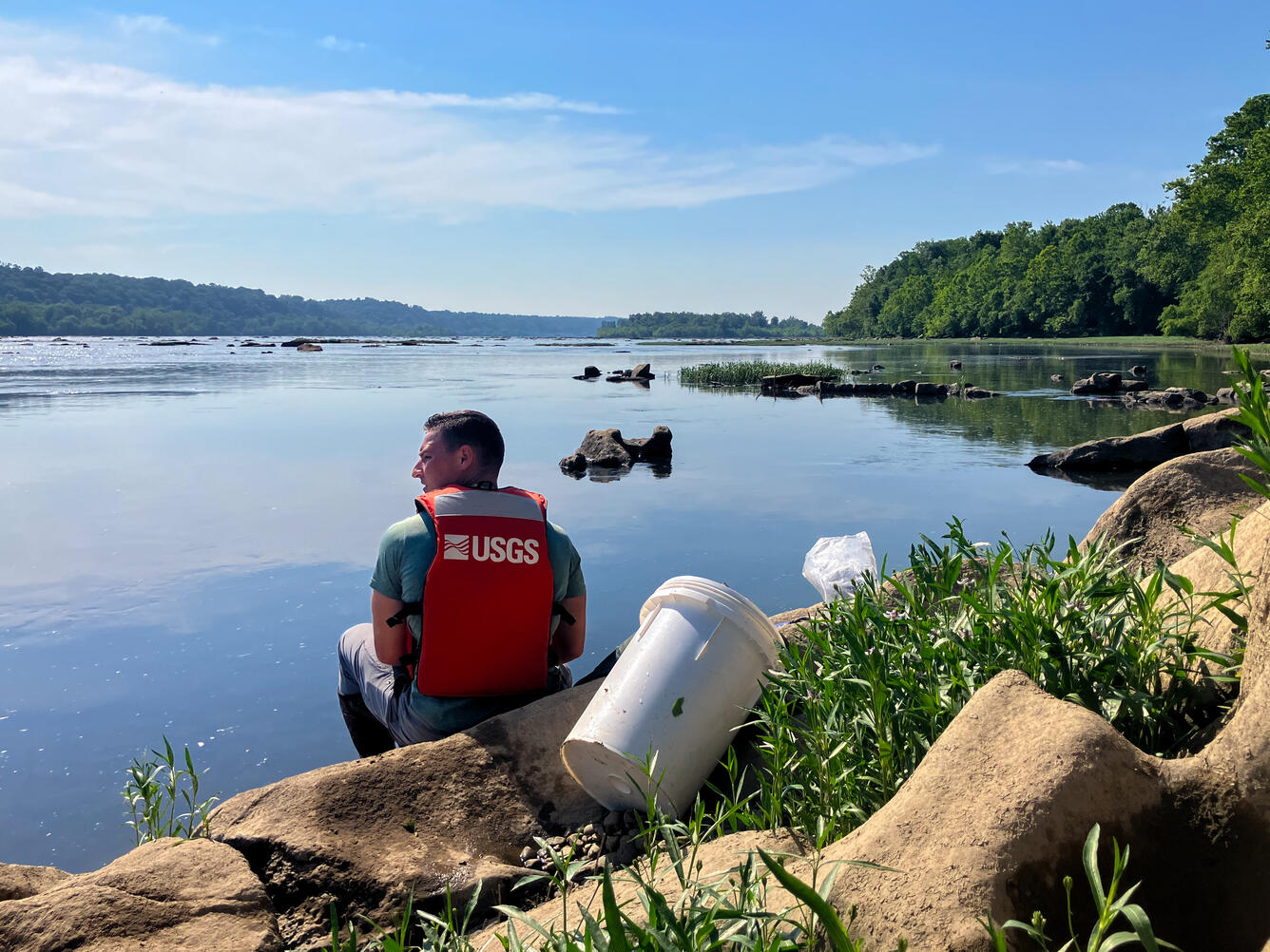 A hydrologic technician sits at the edge of a river.