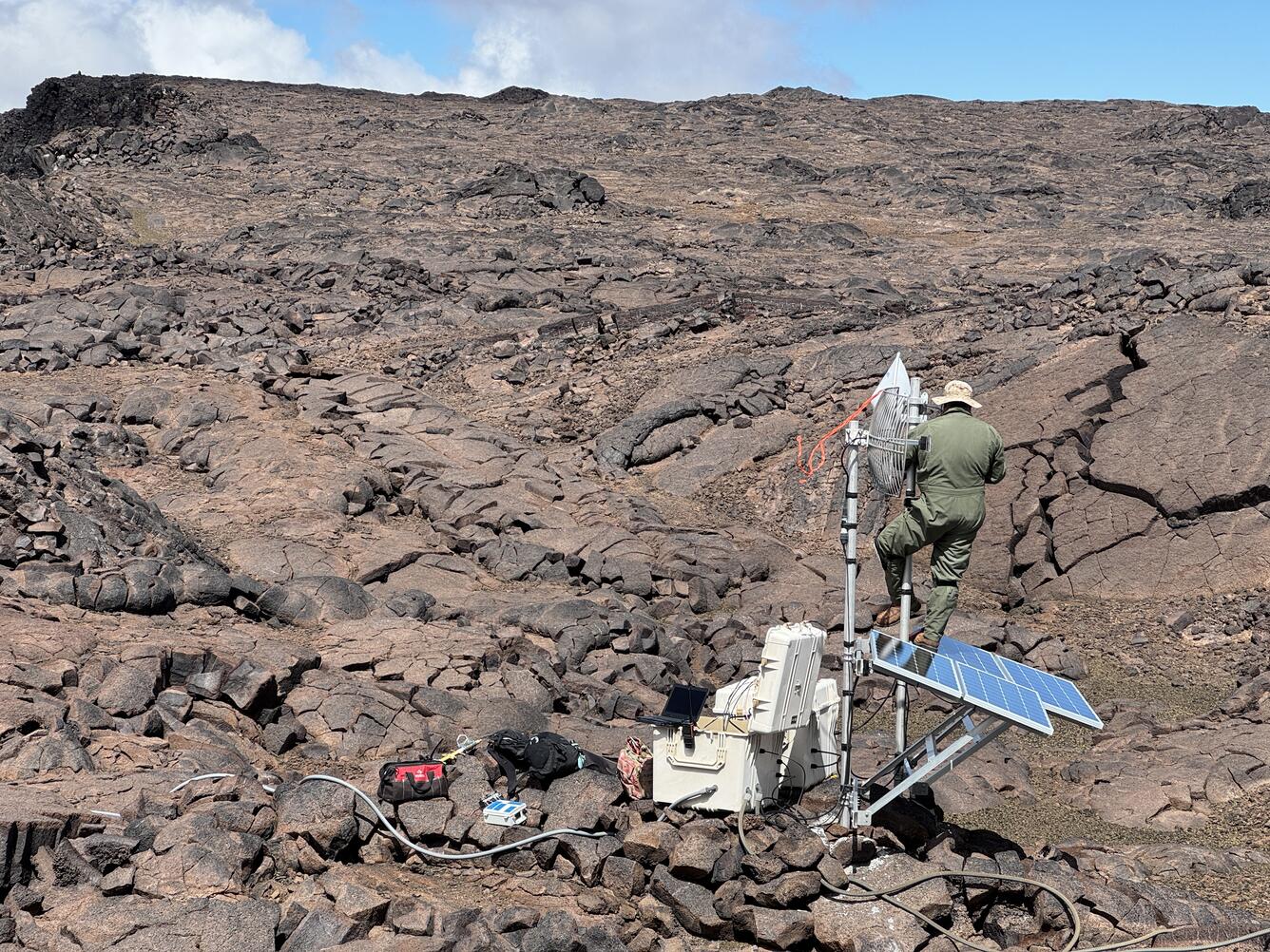 Color photograph of field engineer working on remote volcano monitoring station located on a lava flow