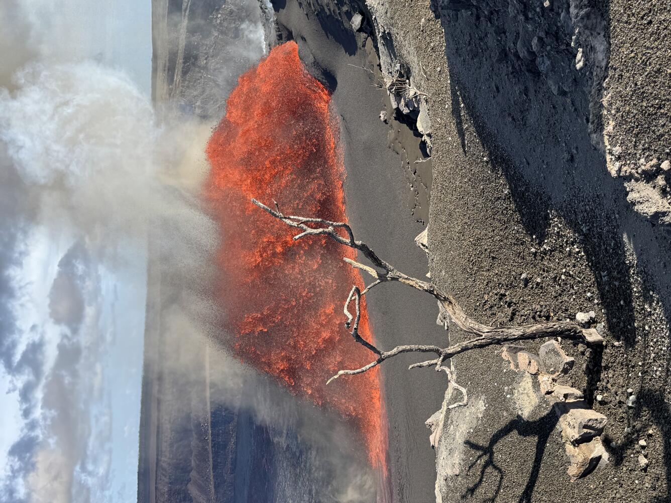 Color photograph of lava fountain with dead tree in foreground