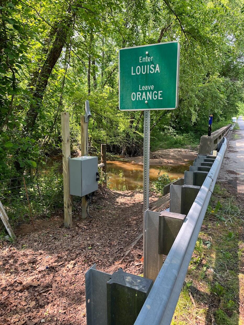 USGS monitoring station next to Roadside signpost stating entering Louisa, leaving Orange 