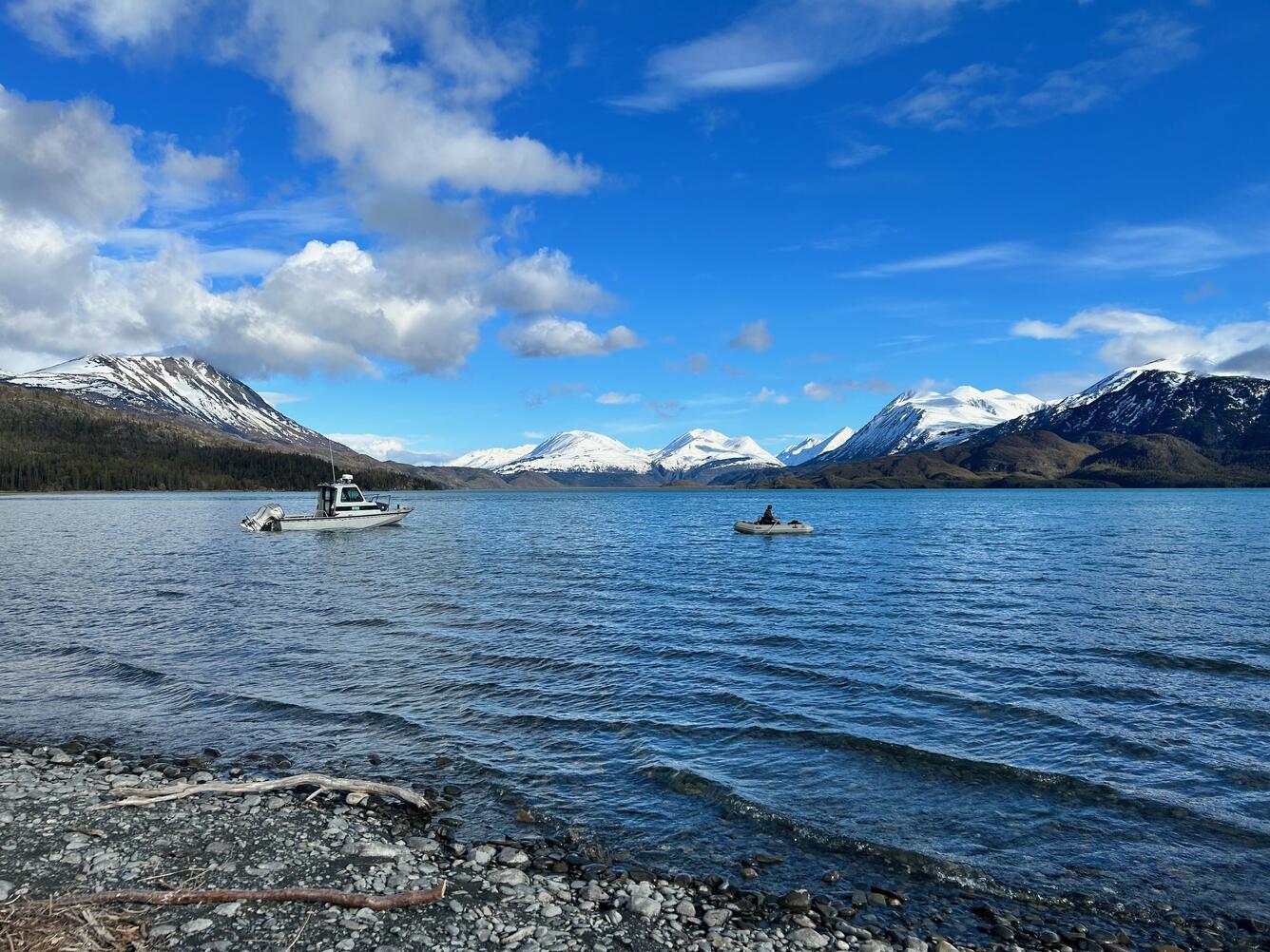 Two boats sit in a lake with snow capped mountains in the background