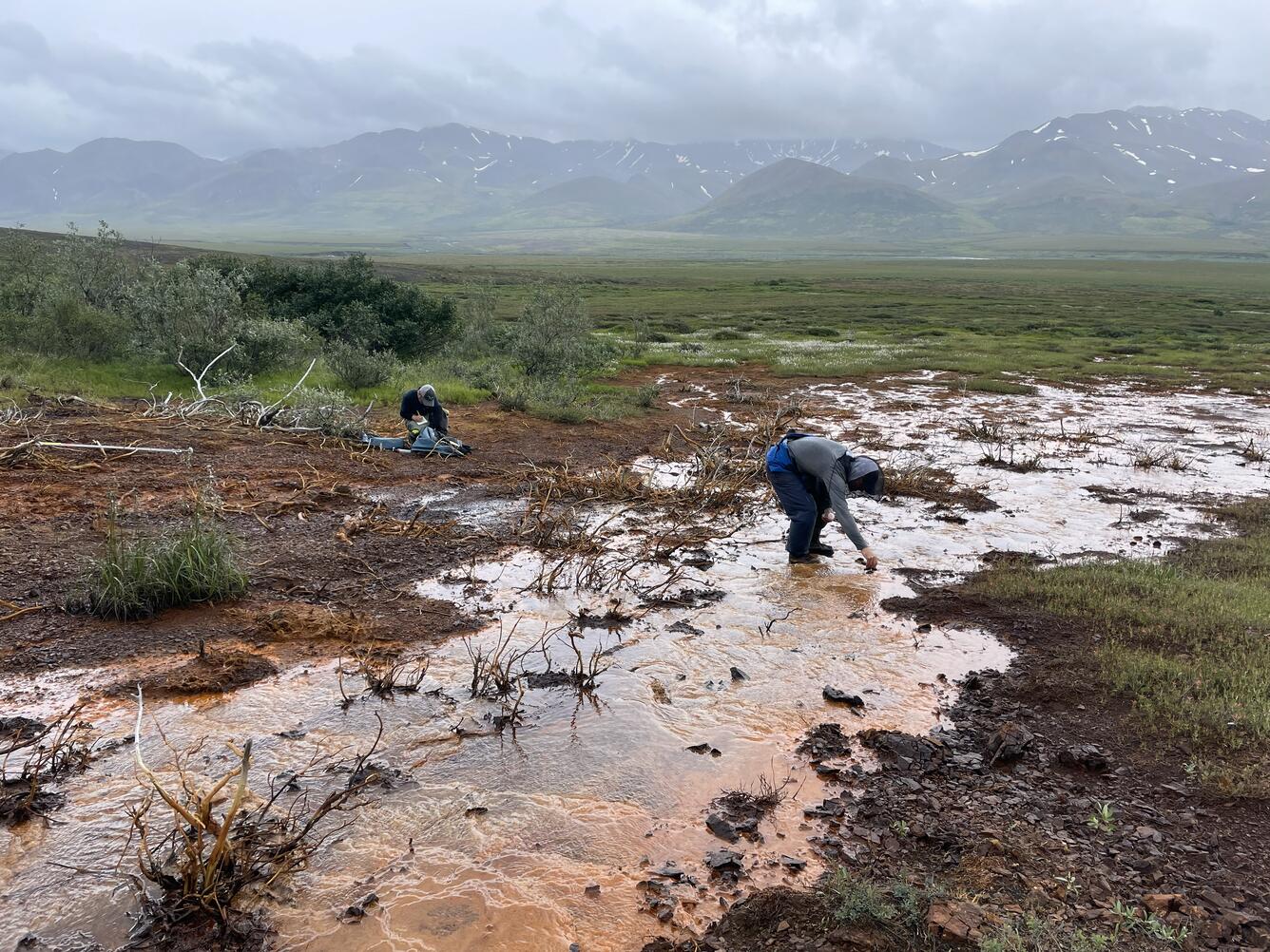 Two people sampling water from an orange creek.