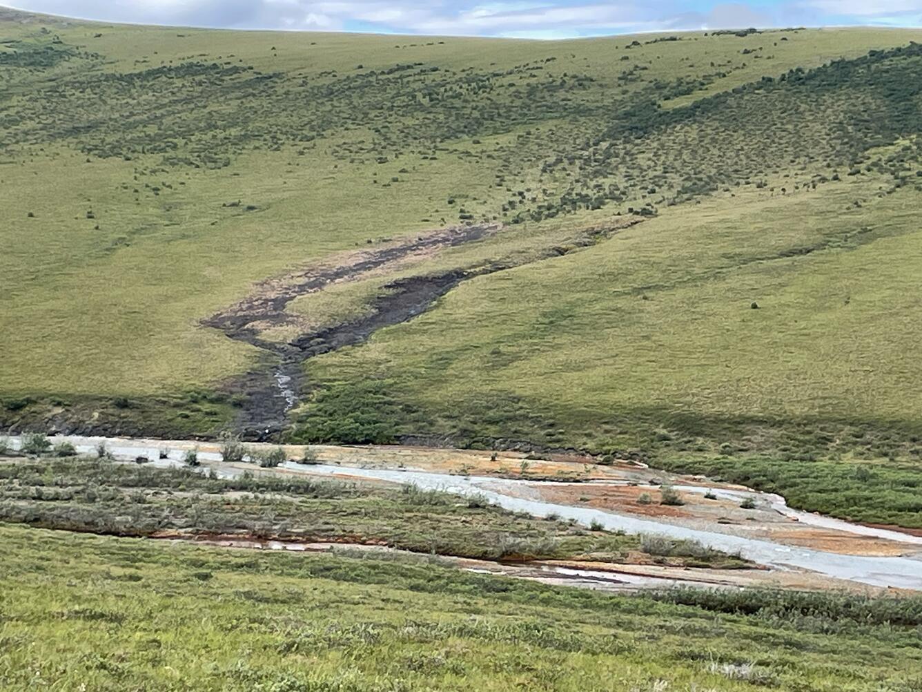 A blue creek running down a hillside into an orange river.