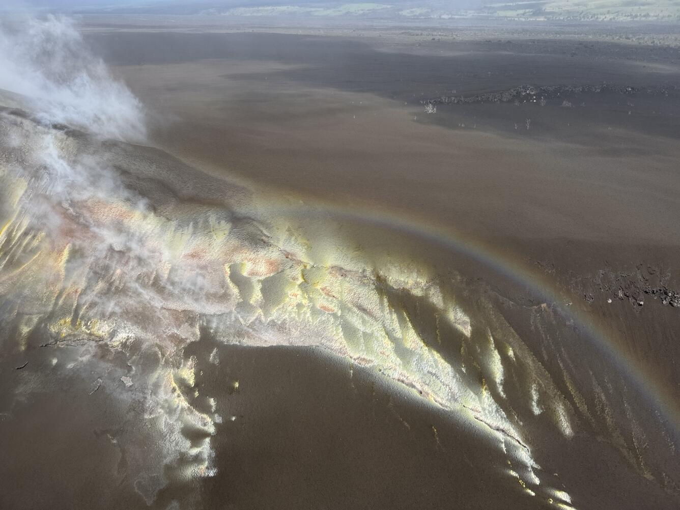 Color photograph of sulfur deposits on crater rim, with rainbow