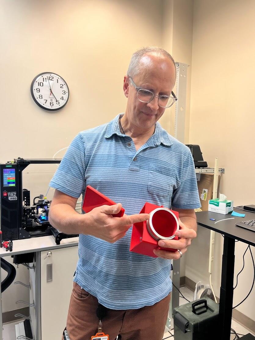 A person holds out a boxy red device made with a 3D printer