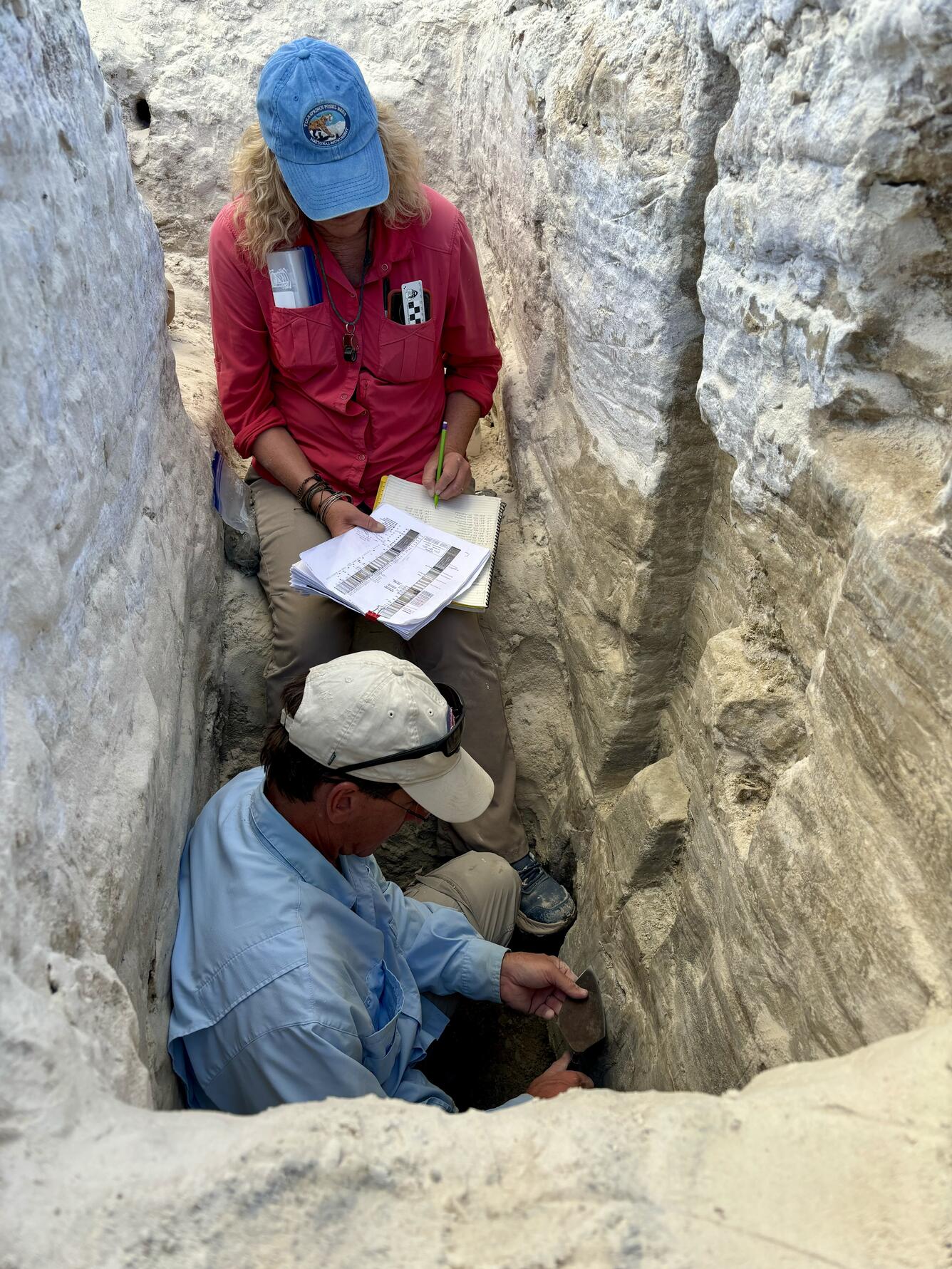 Two people examine sediment layers in a trench