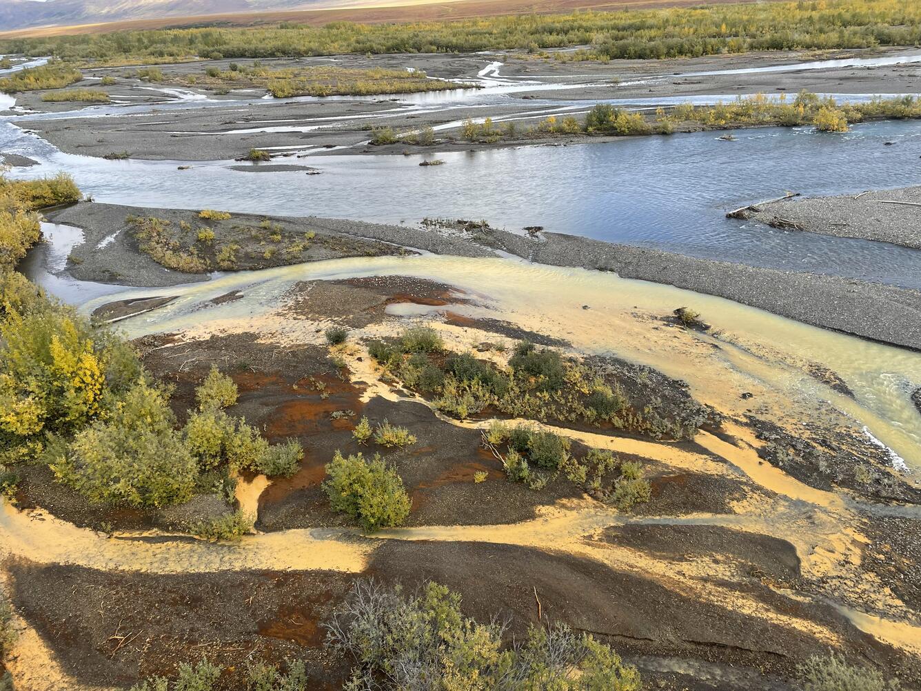 Pale orange creek flowing into clear blue river.