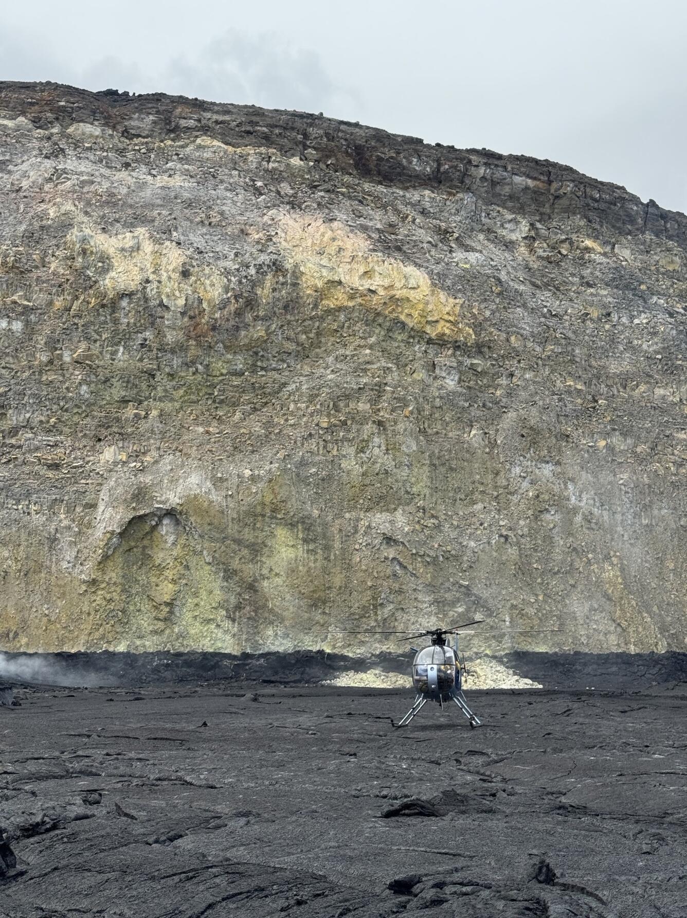 Color photograph of helicopter on crater floor with crater wall in background