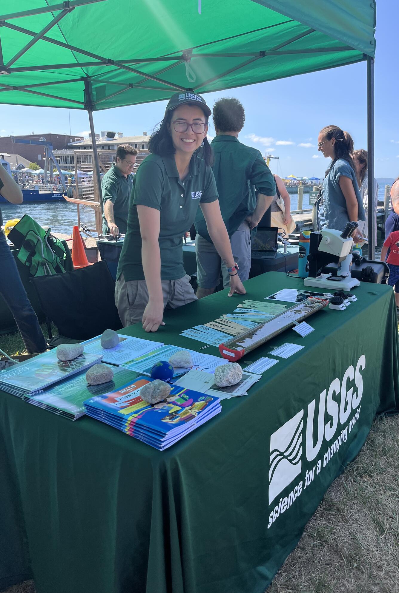 person standing behind USGS booth outside under tent