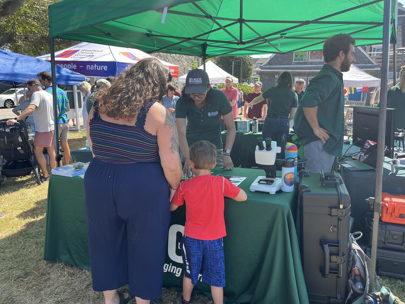 person behind USGS booth talking to adult and child outside under tent