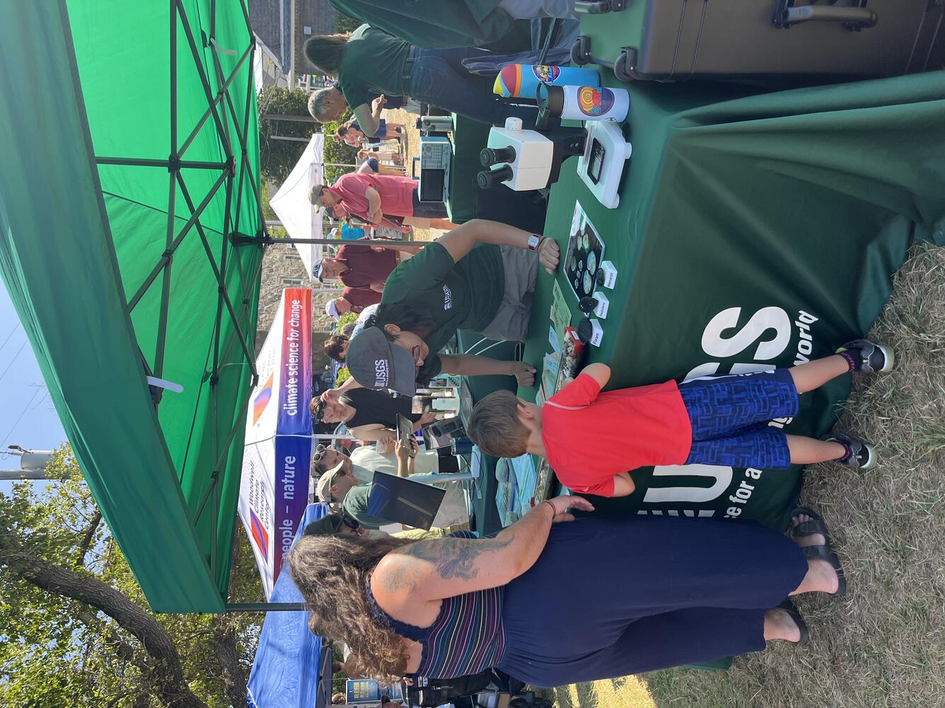 person behind USGS booth talking to adult and child outside under a tent