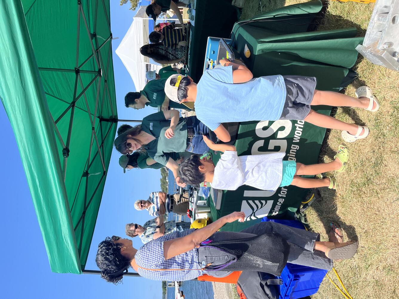 Person in USGS shirt talking to adult and two kids at USGS booth outside
