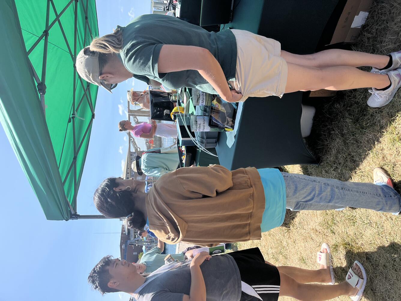 USGS scientist talking to two young adults at USGS booth outside under a tent