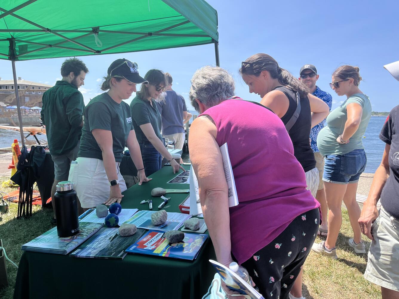People in USGS shirts behind booth outside under tent talking to visitors