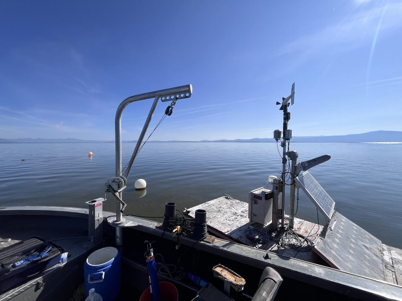 boat with equipment pulls up to floating platform housing water-quality instruments on a bright blue summer day